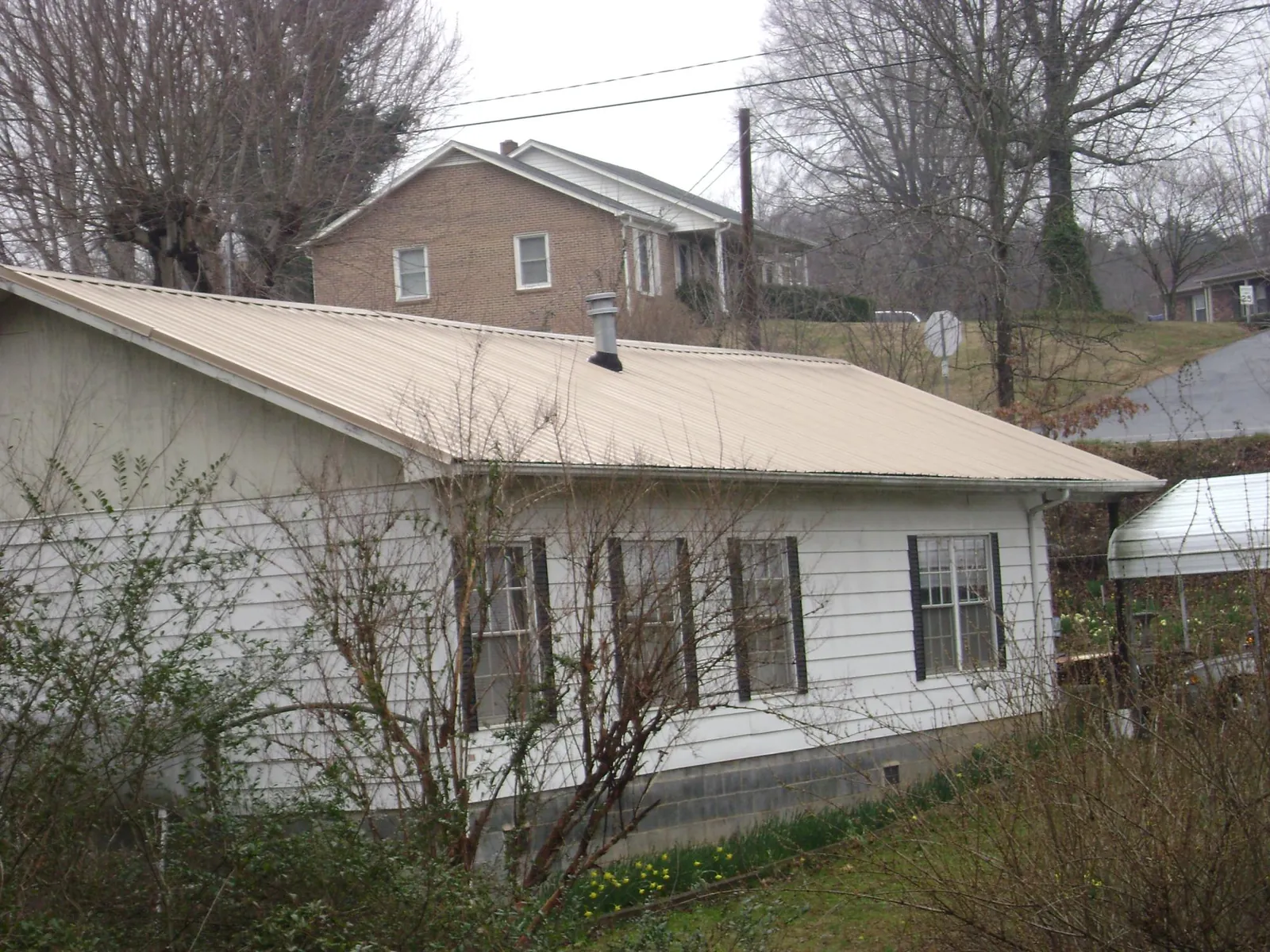 Tan metal roof on a white sided house set into a hillside — Commercial Roofing by Roofing Brothers in Oak Hill